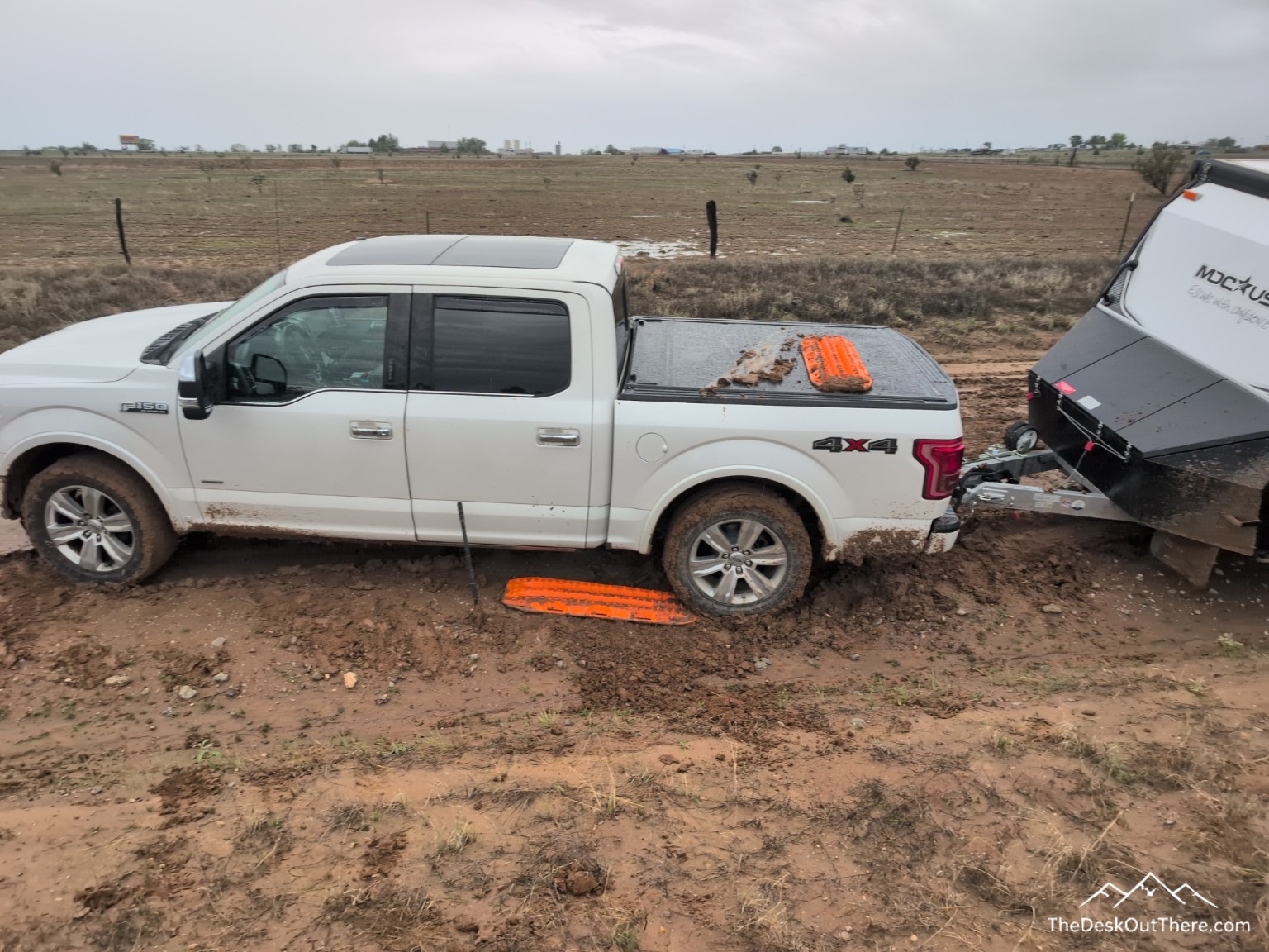 White pickup stuck in mud with an orange recovery board beside the rear tire.
