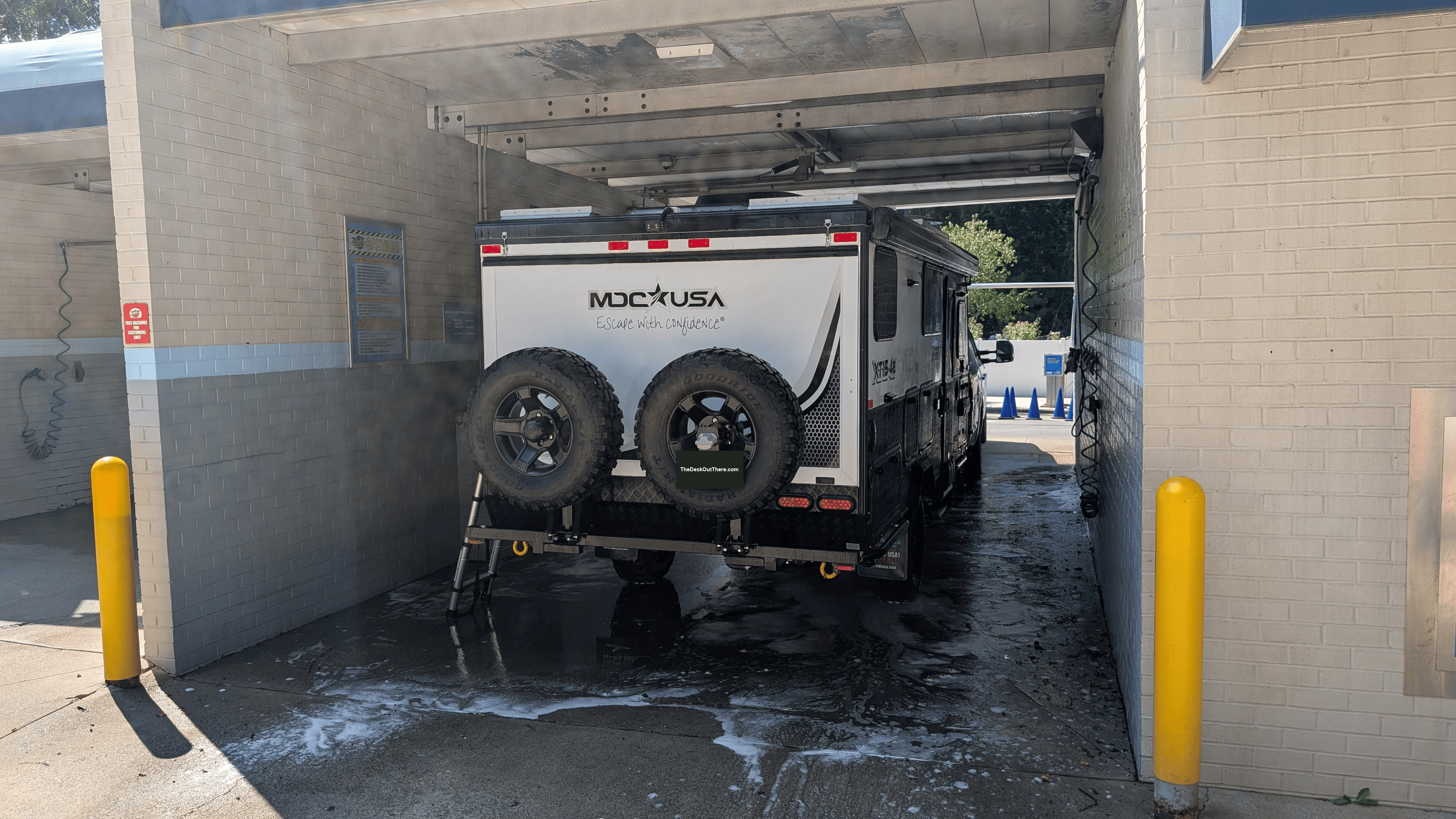Rear view of camper trailer being cleaned in a wash bay, with the license plate covered.