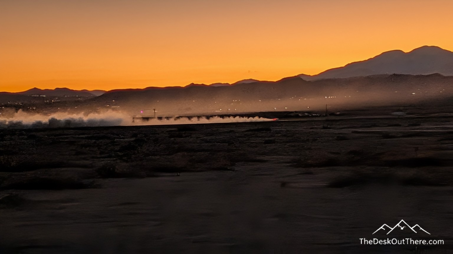 Sunset over the desert mountains with a car raising a trail of dust