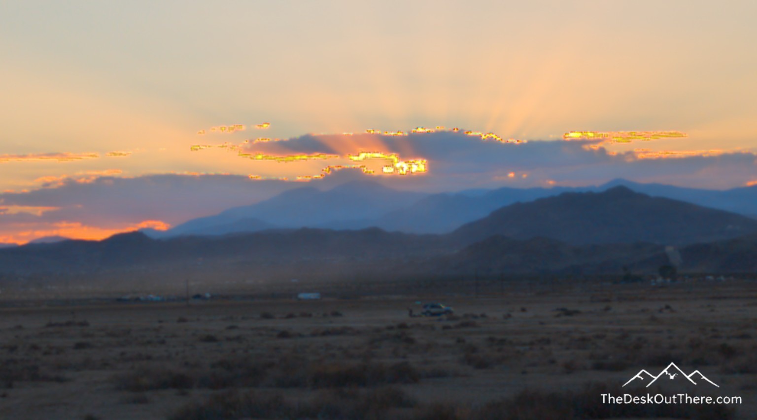Sun setting behind clouds and desert mountains