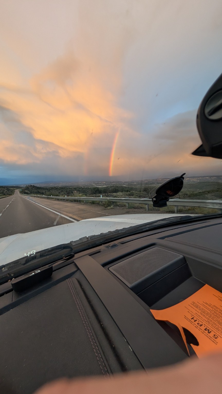 A rainbow over the Arizona landscape beneath sunset clouds, viewed through the truck windshield.