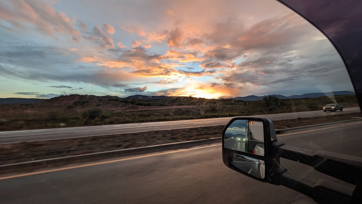 A sunset of pink and orange clouds above the highway viewed from the towing truck.