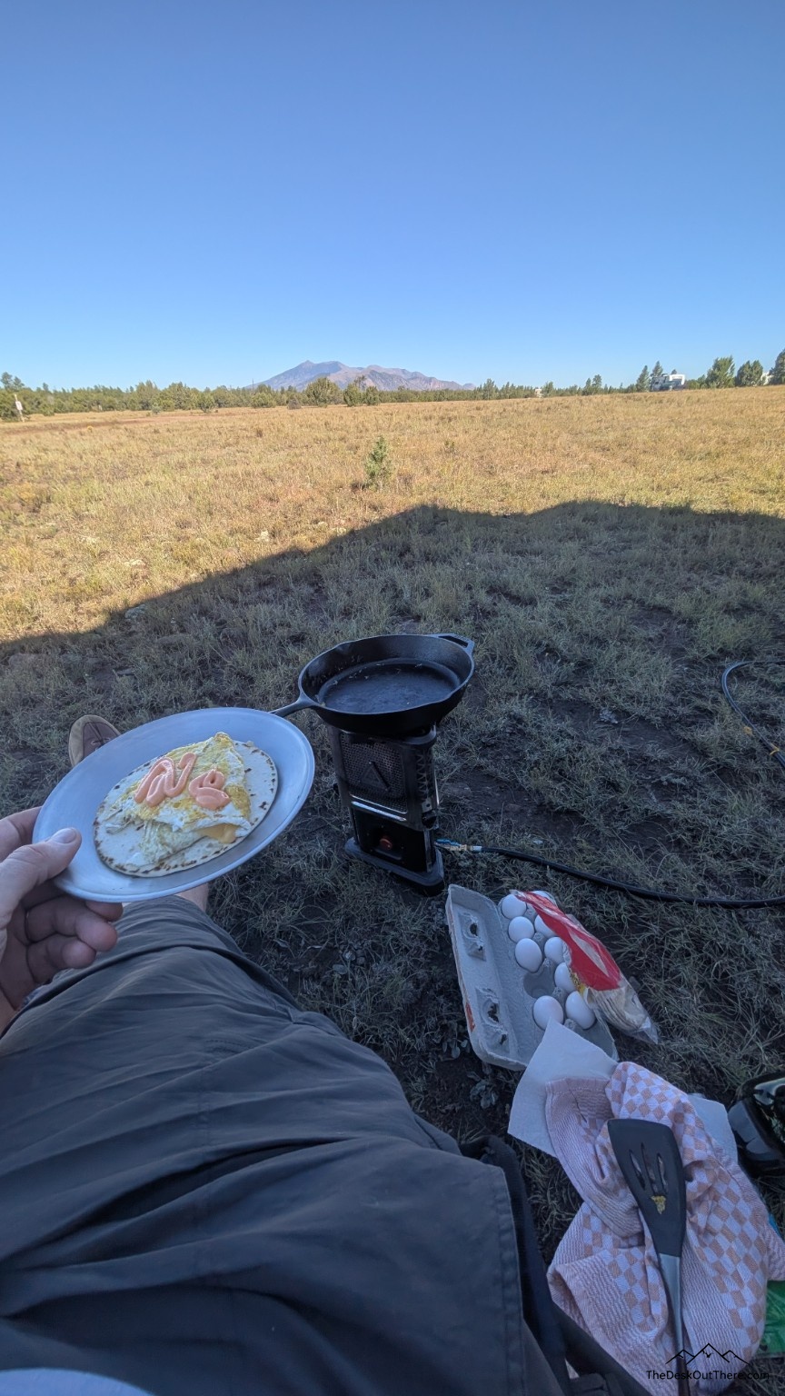 Breakfast cooked outside at camp, with a meadow and mountains in the background.