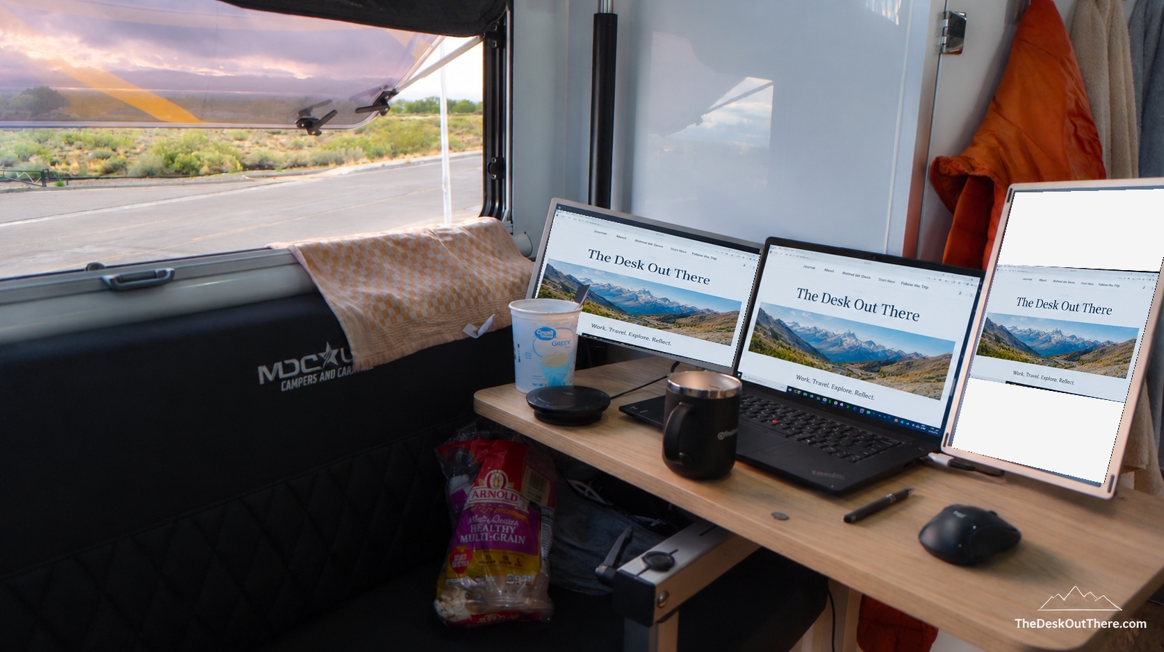 Three-screen workspace inside the camper, with the same The Desk Out There homepage image on each display.